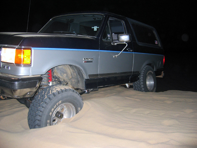 Black and gray Ford Bronco on sand dunes at night with mud tires