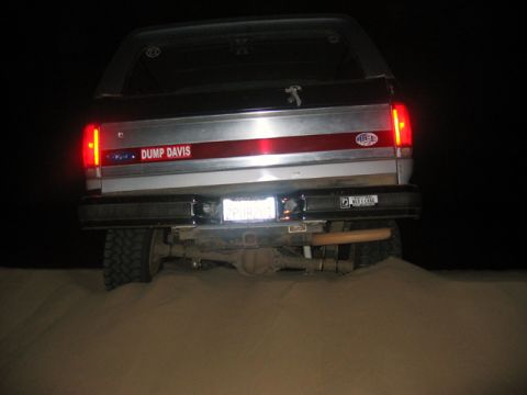 1989 Ford Bronco - This lifted Ford Bronco is stuck in the sand at night, its rear lights glowing.