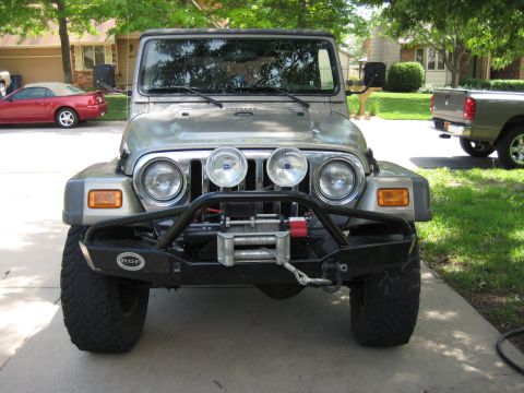 2005 Jeep Wrangler - Head-on view of a khaki Jeep Wrangler with a black soft top in a residential driveway, fitted with a black aftermarket front bumper with st…