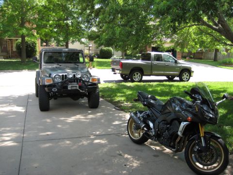 2005 Jeep Wrangler - Khaki Jeep Wrangler with a black winch bumper, stinger hoop and four round auxiliary lights parked in a shaded suburban driveway, viewed fr…