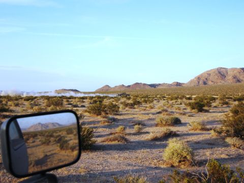 1986 Ford Bronco - A truck drives through a dusty desert landscape under a clear blue sky.