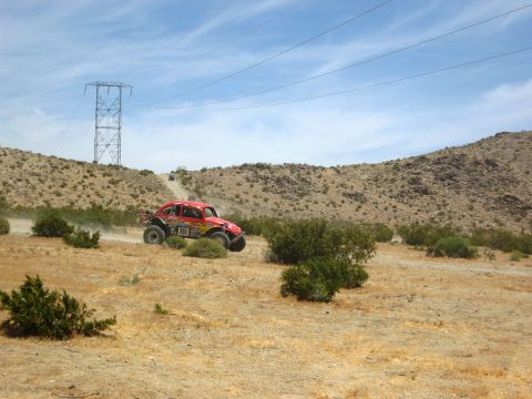 1986 Ford Bronco - A desert race buggy navigates a dusty course under a bright blue sky with power lines in the background.