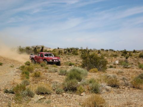 1986 Ford Bronco - A red off-road truck races through a dusty desert landscape under a bright blue sky.