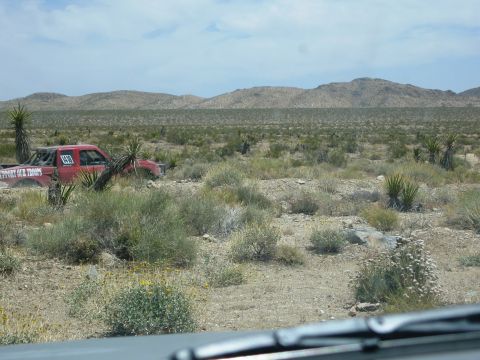 1986 Ford Bronco - A red pickup truck with racing decals is seen in a desert environment, possibly participating in an off-road event.