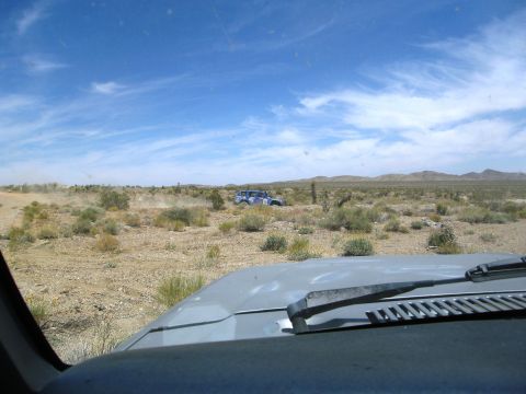 1986 Ford Bronco - Off-road vehicles traverse a dusty desert landscape under a bright blue sky with scattered clouds.
