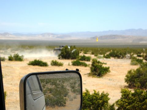 1986 Ford Bronco - Off-road vehicles kick up dust in a desert environment under a clear blue sky.