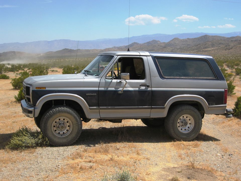 Side view of a two-tone gray and black Ford Bronco parked on a dirt road in a desert landscape
