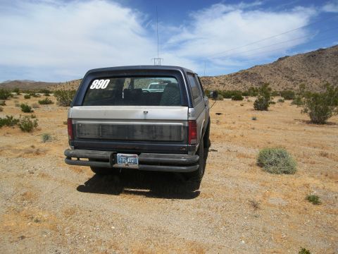1986 Ford Bronco - A Ford Bronco is parked in a dry, desert landscape with mountains in the background.