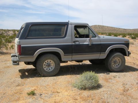 1986 Ford Bronco - This two-tone 1986 Ford Bronco is parked in a dry, arid environment with sparse vegetation.