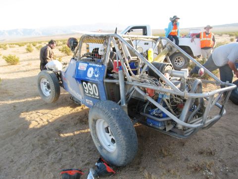 1986 Ford Bronco - A blue off-road buggy, numbered 990, is seen in a desert environment with a support truck and crew nearby.