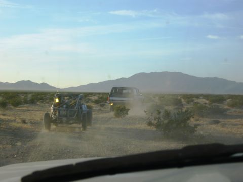 1986 Ford Bronco - Two vehicles kick up dust as they travel through a barren desert landscape under a hazy sky.