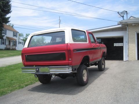 1979 Ford Bronco - Rear view of a red 1978 Ford Bronco with a white top, parked in front of a garage.