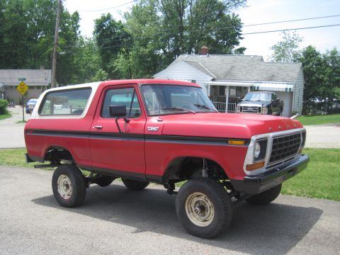 1979 Ford Bronco - This red 1979 Ford Bronco features a lifted suspension and a white removable top, presented in a three-quarter front view.