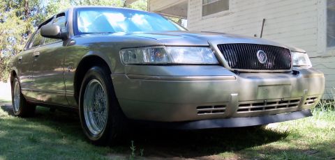 2000 Mercury Grand Marquis - A silver Mercury Grand Marquis is parked outside a building on a sunny day.