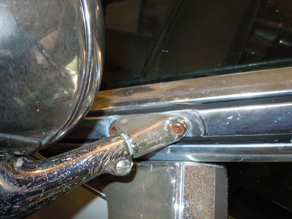 Chrome side mirror mount with visible screws and rust on a dark vehicle