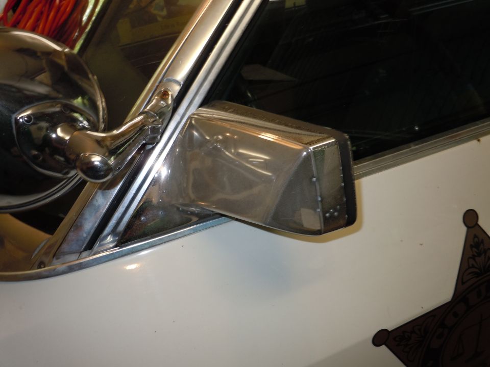 Chrome side mirror assembly on a white vehicle with a partial star emblem visible