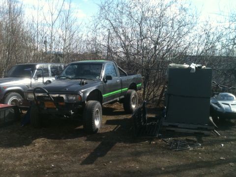 2001 Ford F-350 - A modified Toyota pickup truck is parked outdoors next to another vehicle and some storage containers.