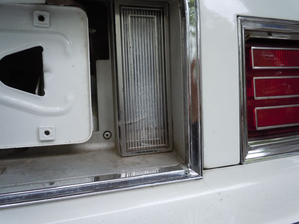 Close-up of a white car's rear light assembly, showing a cracked amber reflector and part of a red taillight