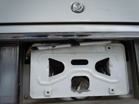 2001 Ford Crown Victoria - The rear of a white vehicle shows a damaged license plate bracket with visible wiring and a trunk lock mechanism above.