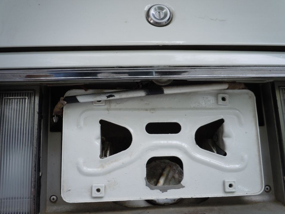 White car's rear bumper with a detached license plate bracket and exposed wiring