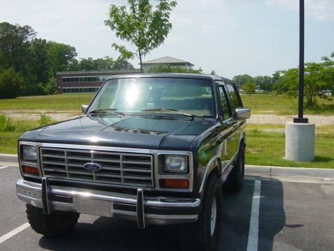 1979 Ford Bronco - This Ford Bronco is parked in a lot with a building and trees in the background.