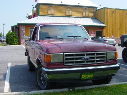 1979 Ford Bronco - This maroon Ford pickup truck, likely from the late 1980s, is parked in front of a building.