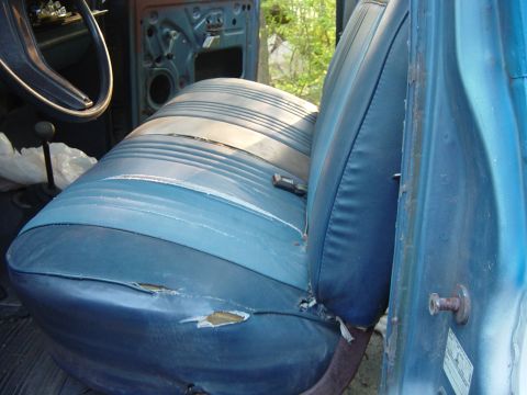 1979 Ford Bronco - The interior of this 1979 Ford Bronco shows significant wear on the blue bench seat, with visible rips and tears.