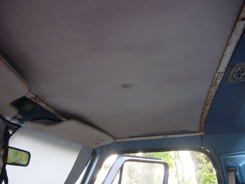 1979 Ford Bronco - The interior of a vehicle shows a worn headliner and sun visor, with a reflection in the side mirror.