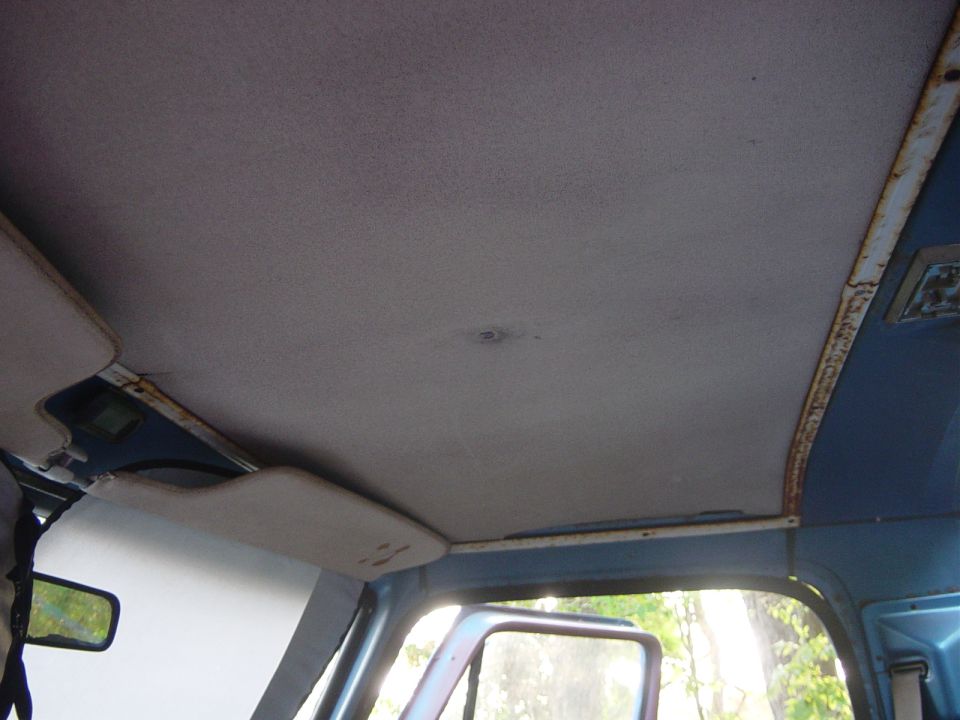 Vehicle interior showing a gray headliner, sun visor, and a reflection in the side mirror