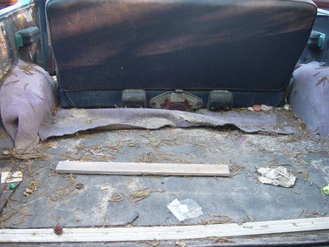 1979 Ford Bronco - The cargo area of a vehicle shows a dirty floor and a folded seat, with debris scattered around.