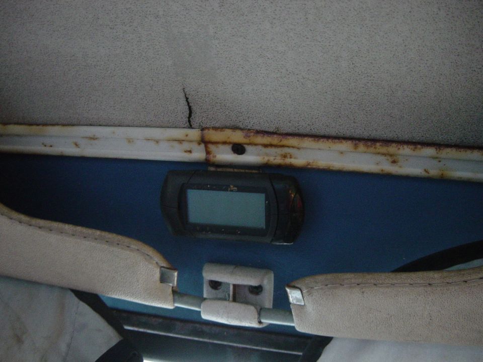 Vehicle interior showing a cracked headliner, rusty trim, and a digital gauge above blue upholstery