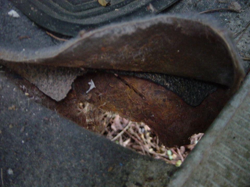 Torn car floor mat showing dirt and debris underneath