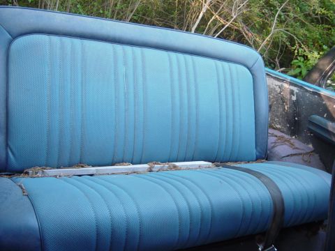 1979 Ford Bronco - The interior of a blue vinyl seat with vertical stitching is visible, showing signs of wear and debris.