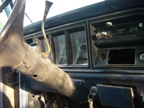 1979 Ford Bronco - The interior of a vintage truck shows a worn dashboard with a column shifter and climate controls. Keys are in the ignition.