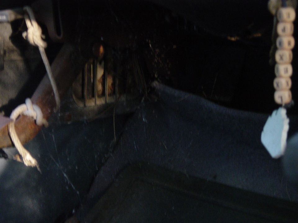 Interior of a dark vehicle with cobwebs, showing a vent and a beaded string with a white charm hanging