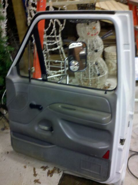 1979 Ford Bronco - Interior of a vehicle door panel, showing the gray trim, handle, and speaker grille.