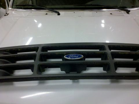 1979 Ford Bronco - A close-up of a Ford grille with the blue oval emblem is shown against a white vehicle's hood.