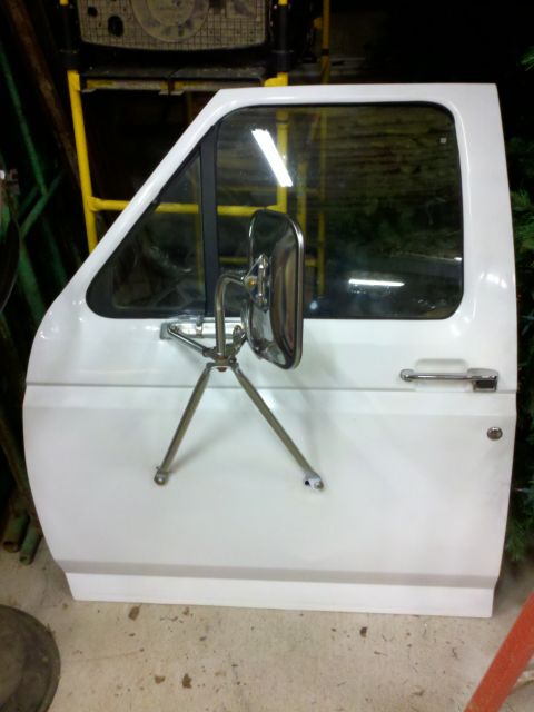 1979 Ford Bronco - A detached white truck door with a large chrome side mirror is shown indoors.