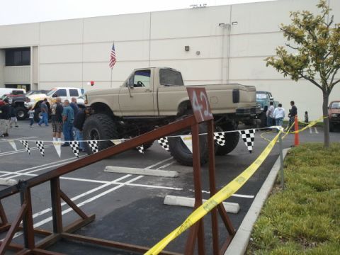 1978 Ford Bronco - A modified pickup truck with oversized tires is parked at an outdoor event, with spectators and racing flags visible.