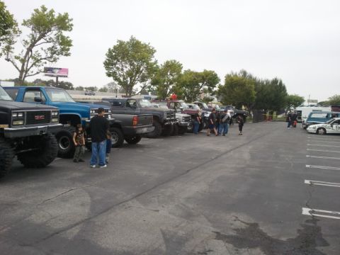 1978 Ford Bronco - A variety of trucks and cars are parked in a lot, with people milling around.