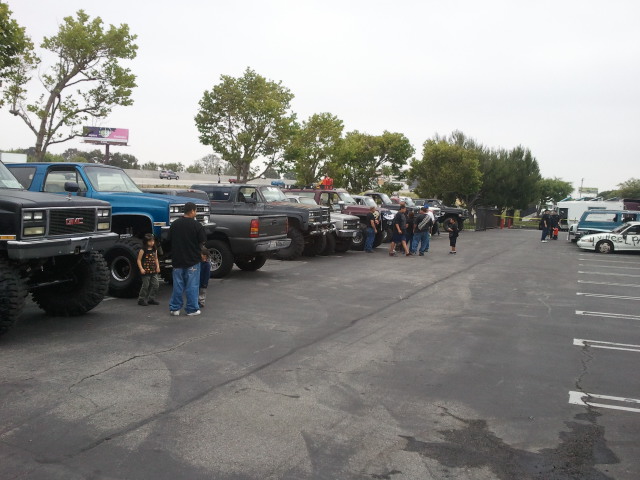 Several lifted trucks and cars parked in a lot under an overcast sky