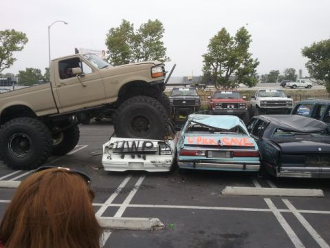 1978 Ford Bronco - Monster truck crushing several cars in a junkyard or demolition derby event.