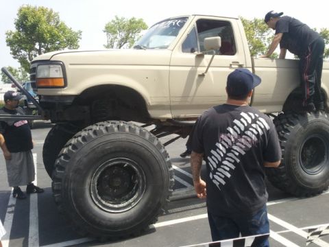 1978 Ford Bronco - A modified pickup truck with oversized tires is parked outdoors, with several people observing it.