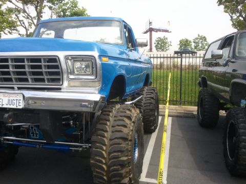 1978 Ford Bronco - A lifted blue pickup truck with oversized tires is parked next to another vehicle.