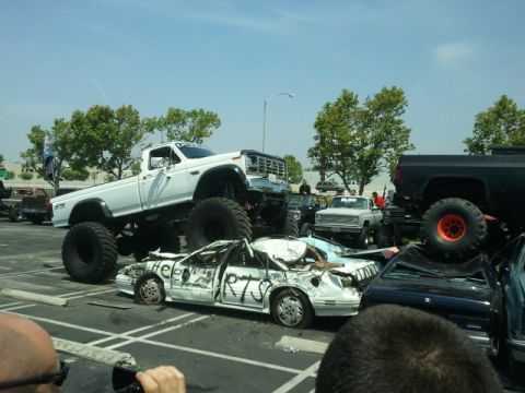 1978 Ford Bronco - A monster truck event shows a white monster truck crushing a white sedan that has 'Help RTS' spray-painted on its side.
