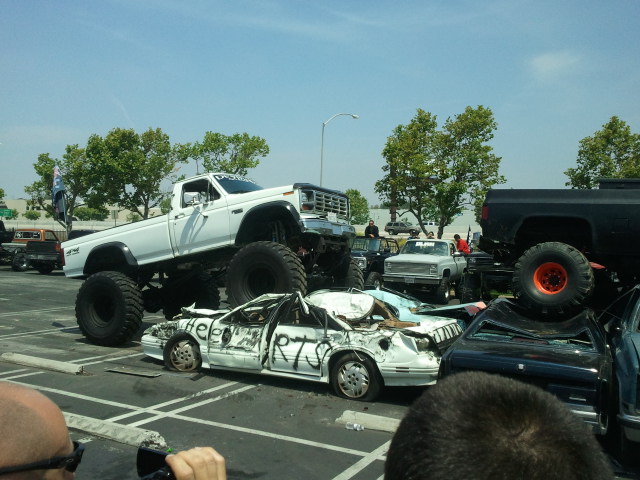 White monster truck crushing a white sedan with 'Help RTS' written on it