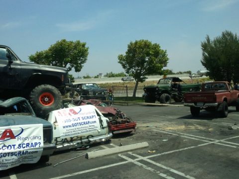 1978 Ford Bronco - Several trucks and wrecked cars are parked in a lot, some with recycling company banners displayed.