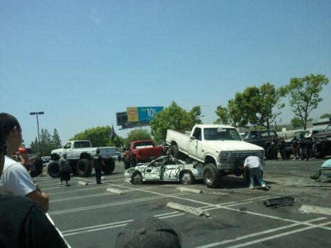 1978 Ford Bronco - A white pickup truck is positioned on top of a heavily damaged car in a parking lot scene.