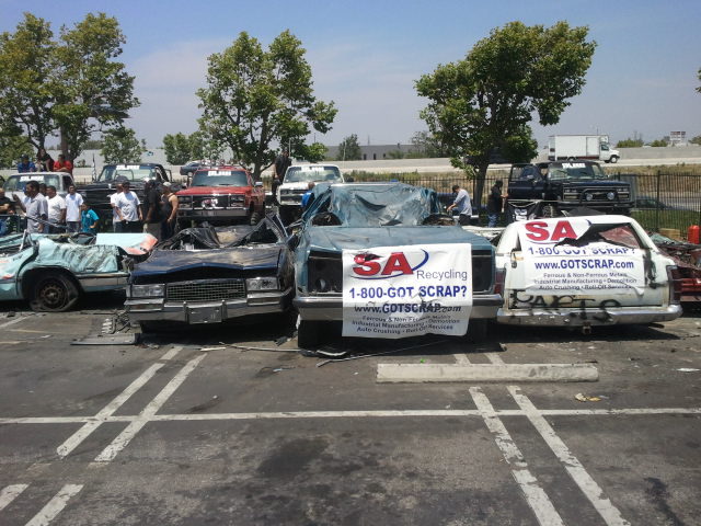 Several wrecked cars in a scrapyard, one with a banner reading "SA Recycling 1-800-GOT SCRAP?"