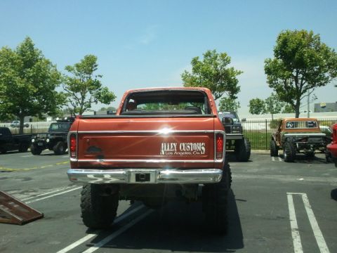 1978 Ford Bronco - Rear view of a lifted orange pickup truck with custom decals on the tailgate.